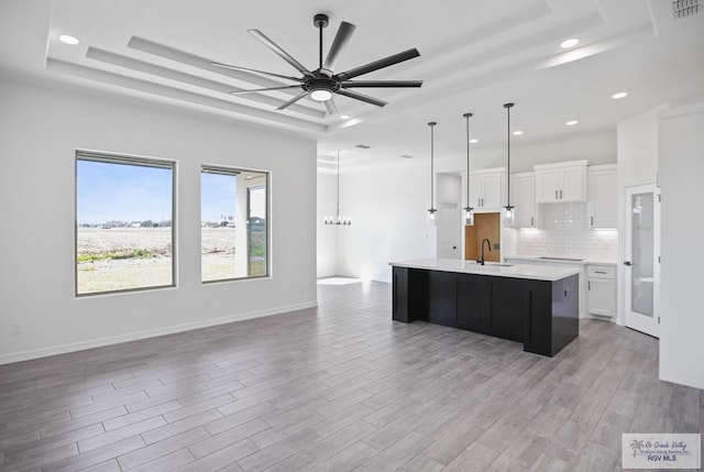 kitchen featuring a sink, white cabinets, light wood-type flooring, a tray ceiling, and tasteful backsplash