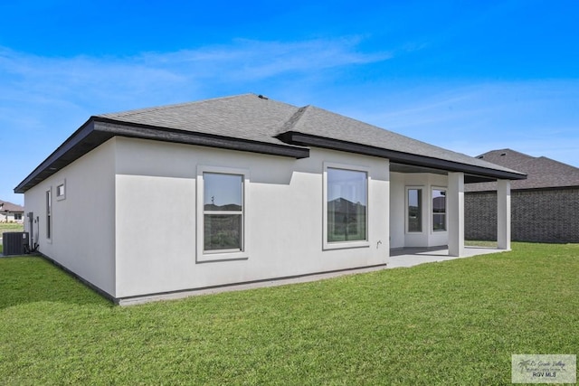 rear view of property with central air condition unit, a patio, a lawn, and roof with shingles