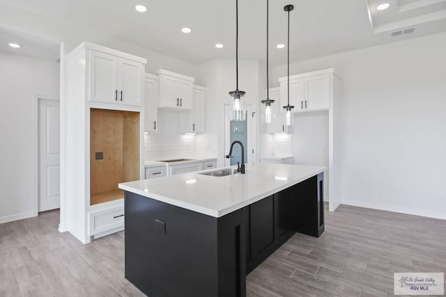 kitchen with tasteful backsplash, white cabinets, a kitchen island with sink, light wood-type flooring, and a sink