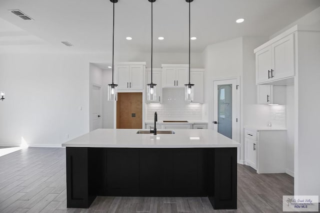 kitchen with light countertops, visible vents, white cabinetry, a sink, and wood finished floors