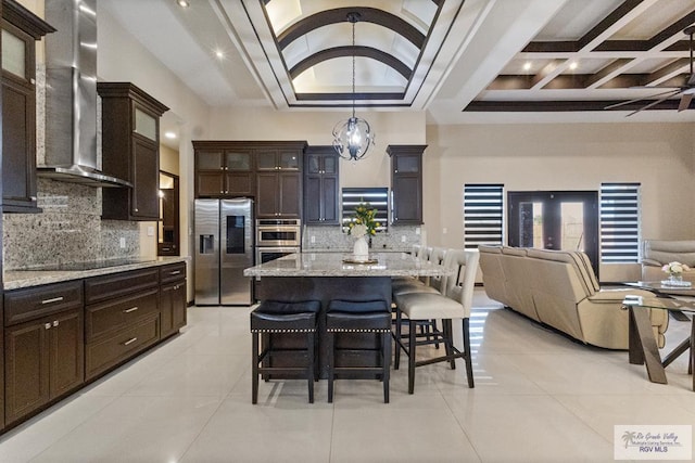 kitchen featuring light tile patterned floors, wall chimney range hood, stainless steel appliances, open floor plan, and coffered ceiling