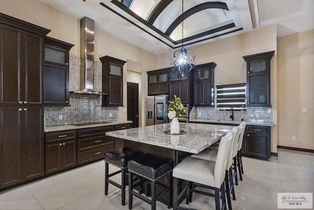 kitchen featuring light tile patterned floors, stainless steel refrigerator with ice dispenser, wall chimney exhaust hood, backsplash, and a kitchen island