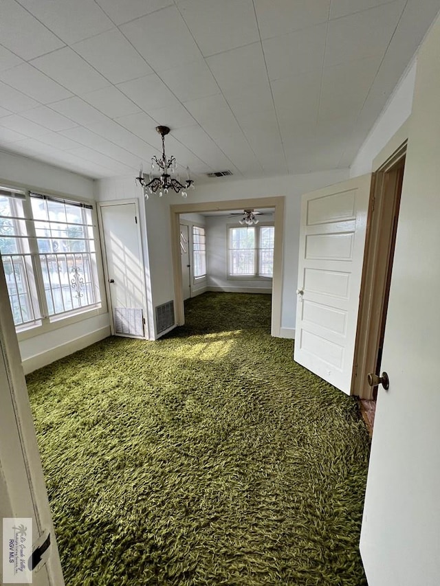 unfurnished room with dark colored carpet, ceiling fan with notable chandelier, and a wealth of natural light