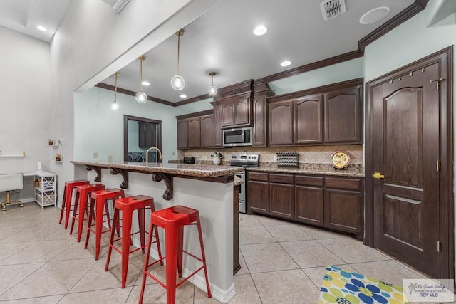 kitchen with light tile patterned floors, a breakfast bar, appliances with stainless steel finishes, hanging light fixtures, and dark brown cabinets