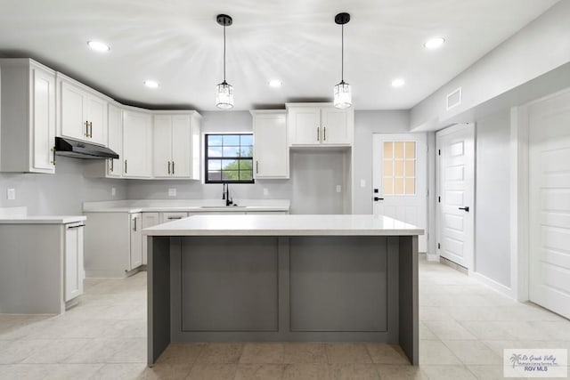 1214 W Monroe Ave, Harlingen, TX 78550 - kitchen featuring under cabinet range hood, a sink, a center island, white cabinets, and pendant lighting