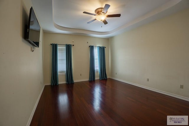 unfurnished room featuring ceiling fan, dark wood-type flooring, and a tray ceiling