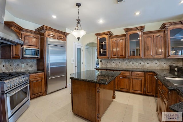 kitchen with decorative backsplash, wall chimney range hood, and high end appliances