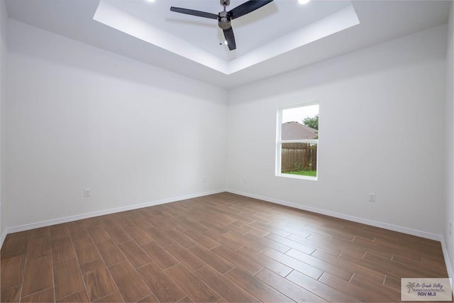 empty room with a tray ceiling, ceiling fan, and dark hardwood / wood-style flooring