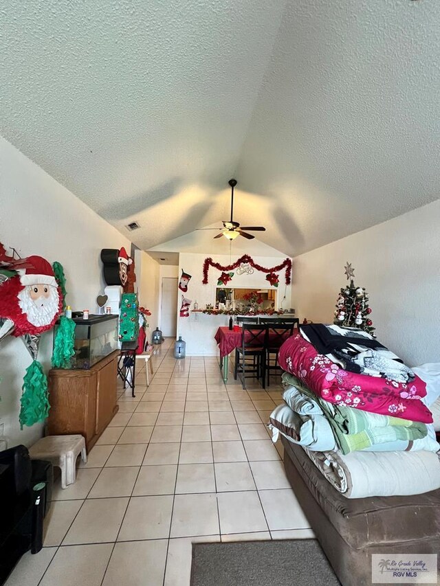 bedroom featuring light tile patterned floors, vaulted ceiling, a textured ceiling, and ceiling fan