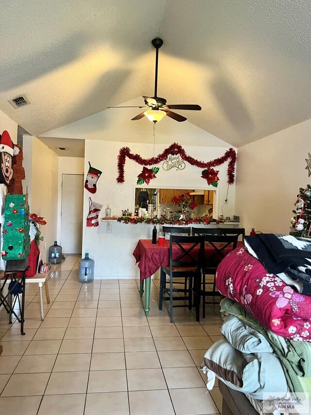 dining area with ceiling fan, tile patterned floors, vaulted ceiling, and a textured ceiling