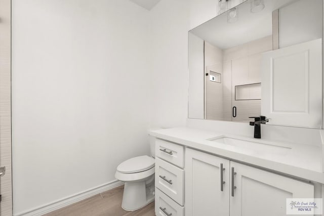 bathroom with toilet, a stall shower, vanity, wood finished floors, and baseboards