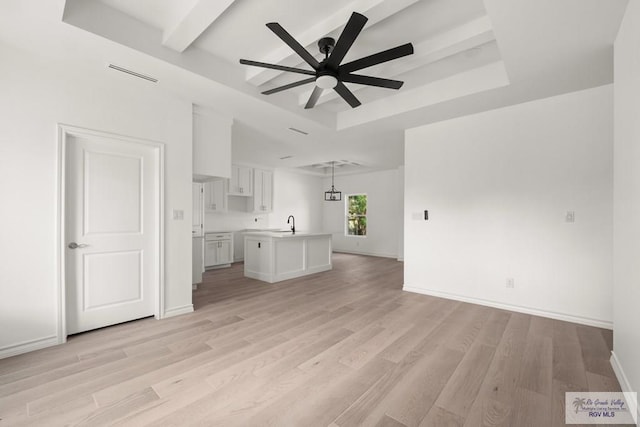 unfurnished living room with light wood-style floors, baseboards, and a raised ceiling