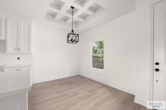 unfurnished dining area featuring light wood-style flooring, baseboards, coffered ceiling, and beam ceiling