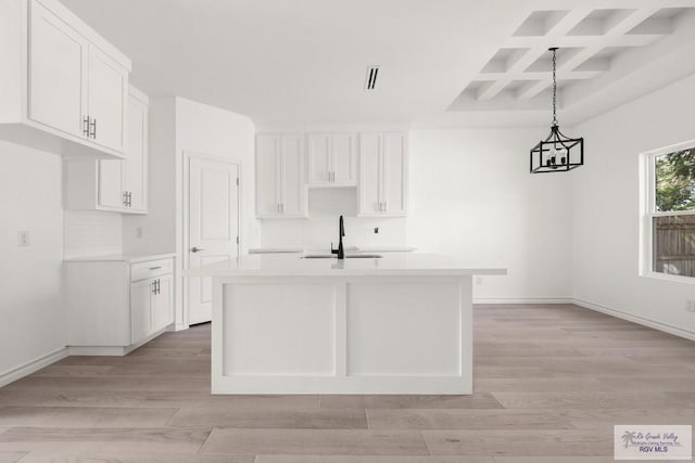 kitchen featuring light countertops, an island with sink, a sink, and pendant lighting