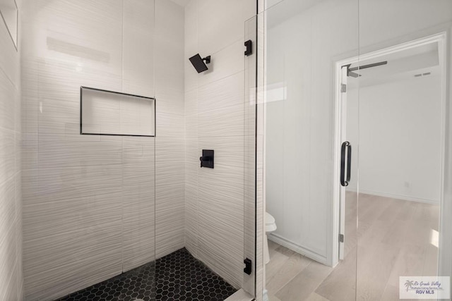 bathroom featuring a shower stall, toilet, and wood finished floors