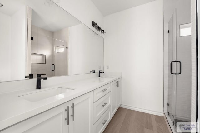 full bathroom featuring double vanity, a shower stall, a sink, and wood finished floors