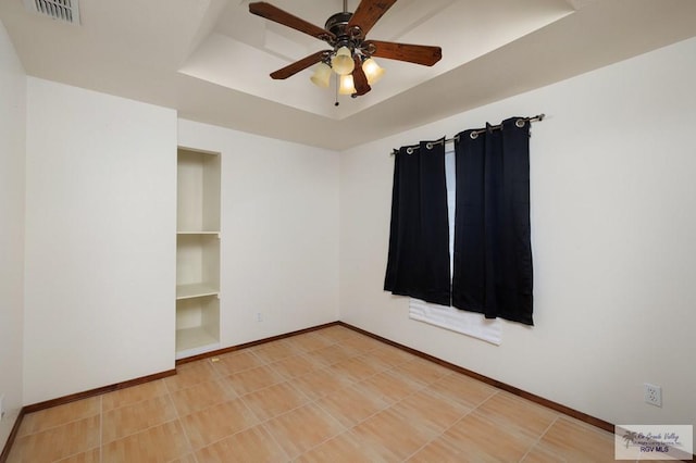 spare room with built in shelves, a raised ceiling, and ceiling fan