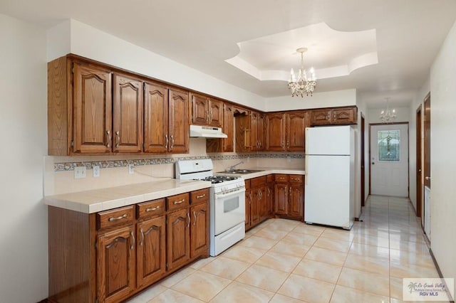 kitchen with decorative light fixtures, white appliances, light tile patterned floors, a tray ceiling, and a notable chandelier