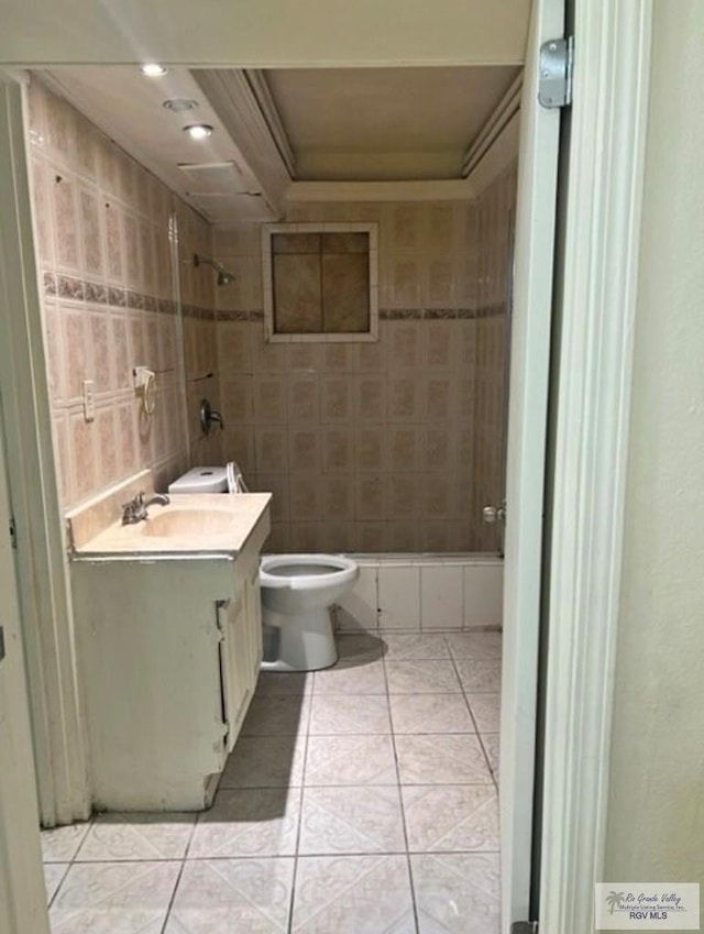 bathroom featuring tile patterned flooring, toilet, tiled shower, vanity, and tile walls