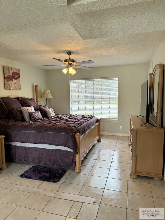 bedroom featuring ceiling fan, light tile patterned floors, and a textured ceiling