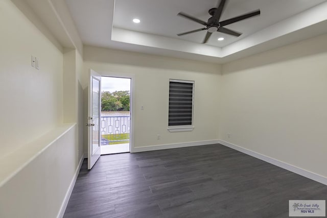 empty room with ceiling fan, a tray ceiling, and dark hardwood / wood-style flooring