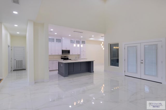 kitchen featuring french doors, decorative light fixtures, appliances with stainless steel finishes, a kitchen island with sink, and white cabinets