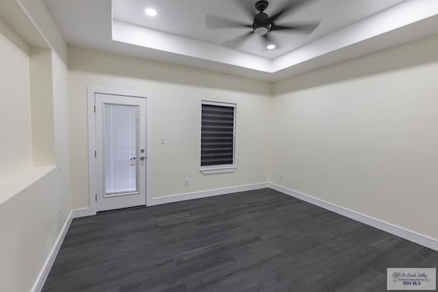 spare room with dark wood-type flooring, ceiling fan, and a raised ceiling