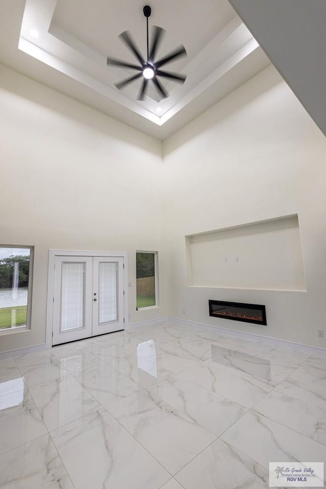 unfurnished living room with french doors, a towering ceiling, ceiling fan, and a tray ceiling