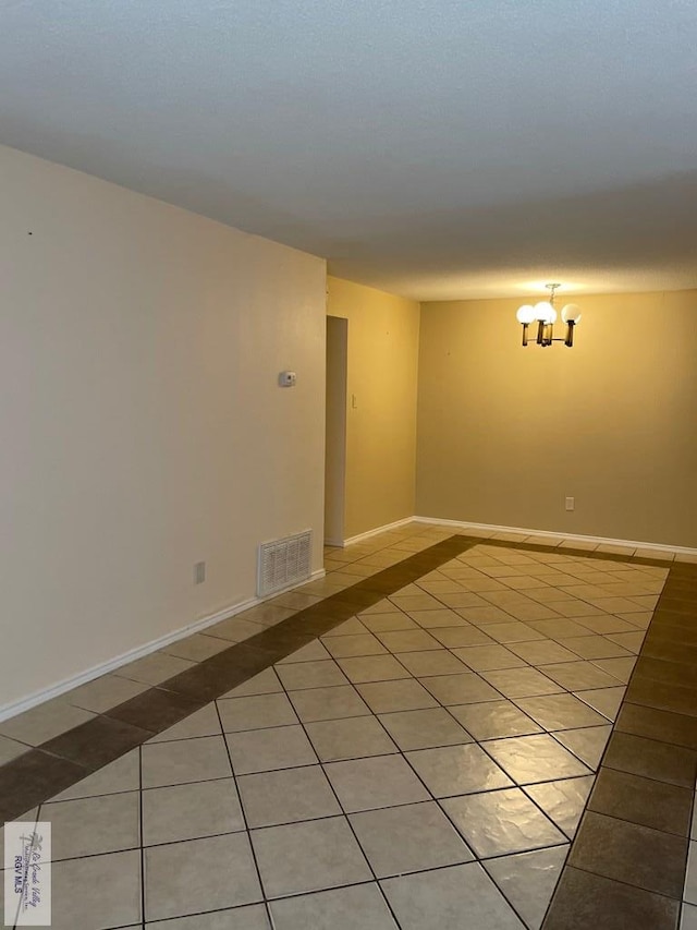 empty room featuring a notable chandelier and light tile patterned flooring