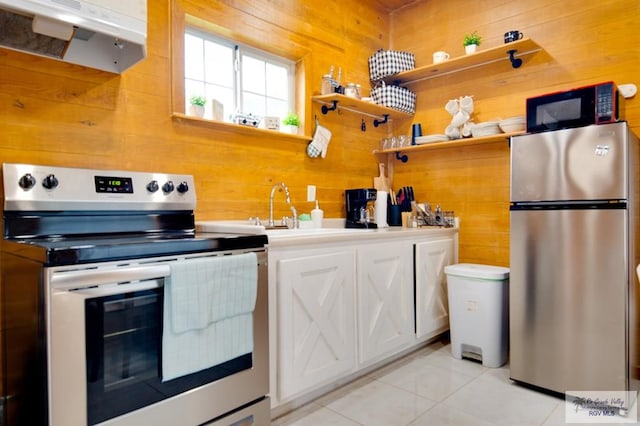 kitchen featuring white cabinetry, range hood, wooden walls, light tile patterned floors, and appliances with stainless steel finishes