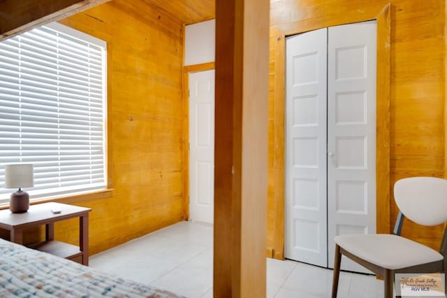 tiled bedroom featuring multiple windows, wooden walls, and a closet