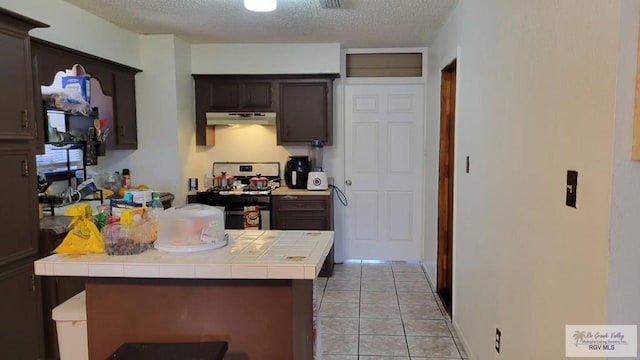 kitchen featuring light tile patterned floors, tile counters, a textured ceiling, gas range, and under cabinet range hood