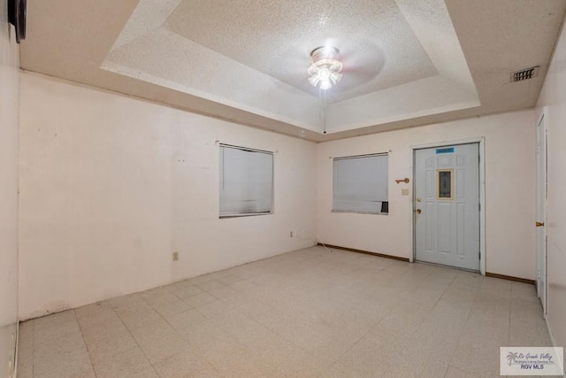 empty room with light floors, visible vents, a raised ceiling, and a textured ceiling