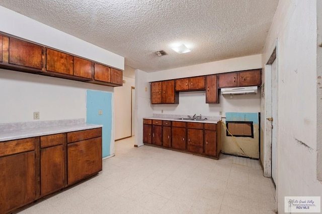 kitchen featuring light floors, light countertops, stove, a sink, and under cabinet range hood