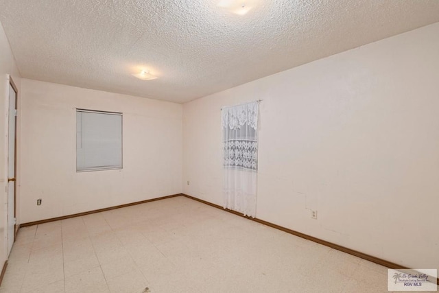 empty room with a textured ceiling, light floors, and baseboards