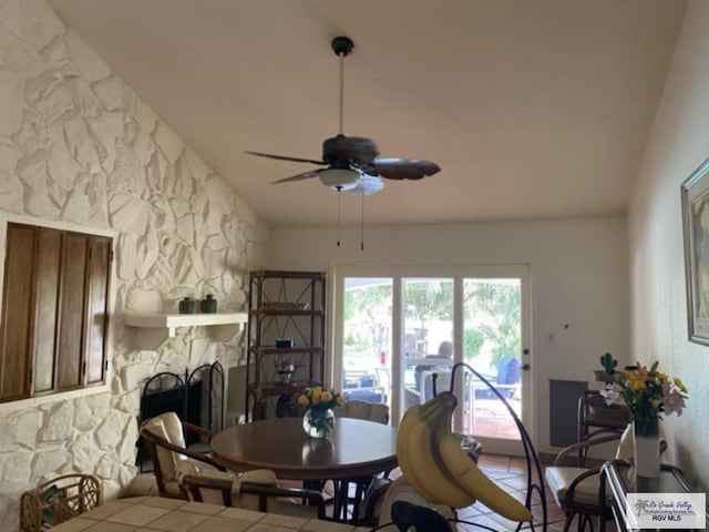 dining area with ceiling fan, a stone fireplace, and lofted ceiling