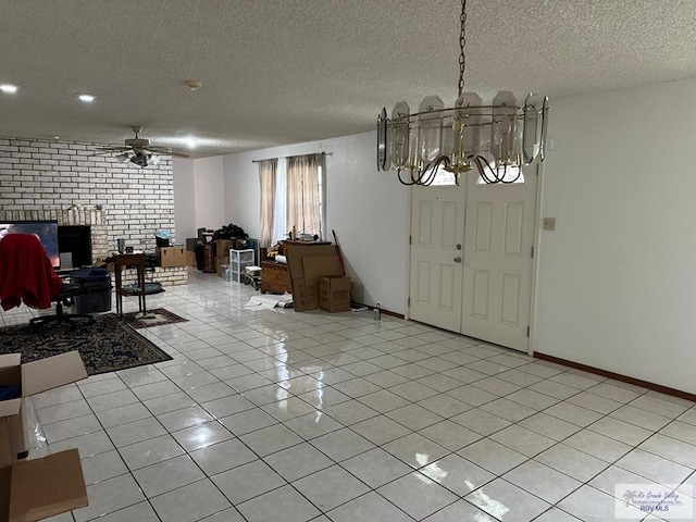 entryway with ceiling fan with notable chandelier, a brick fireplace, light tile patterned floors, and a textured ceiling