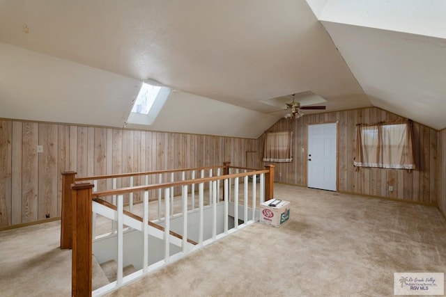 bonus room featuring ceiling fan, wood walls, light colored carpet, and lofted ceiling with skylight