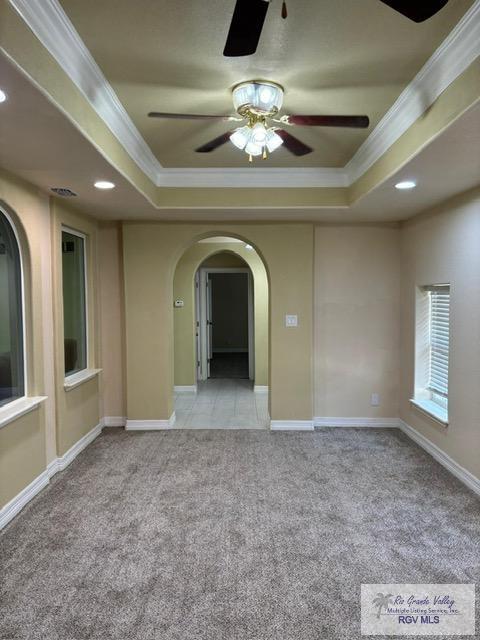 empty room with ornamental molding, light carpet, and a tray ceiling