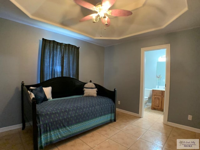 tiled bedroom with ceiling fan, a raised ceiling, and ensuite bath