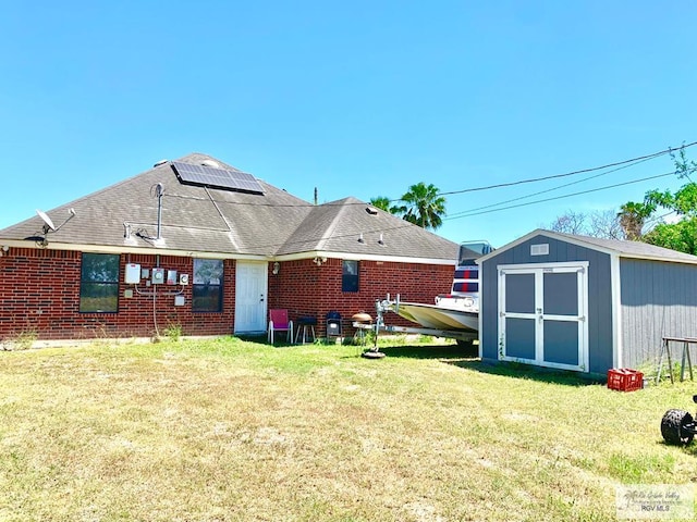 back of house with a lawn, solar panels, and a shed