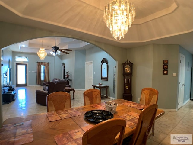 tiled dining space with ceiling fan with notable chandelier and a tray ceiling