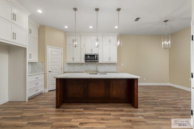 kitchen with hardwood / wood-style floors, backsplash, a center island with sink, and pendant lighting