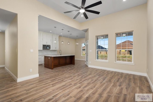 kitchen with white cabinetry, an island with sink, light hardwood / wood-style floors, and decorative light fixtures