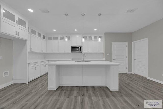 kitchen featuring a center island with sink, white cabinets, hanging light fixtures, and light wood-type flooring