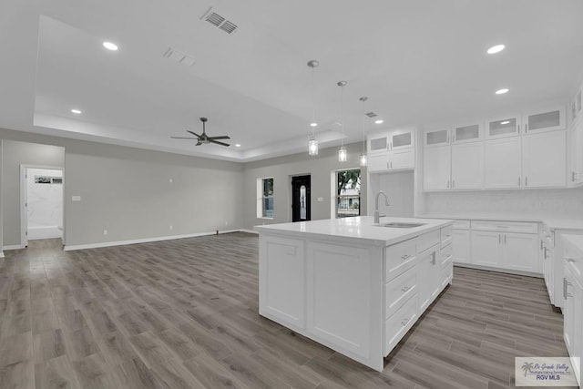 kitchen featuring white cabinets, ceiling fan, an island with sink, and light hardwood / wood-style flooring