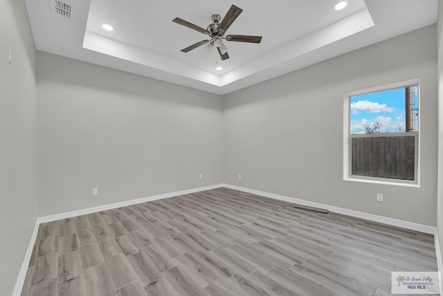 unfurnished room with ceiling fan, light hardwood / wood-style flooring, and a tray ceiling