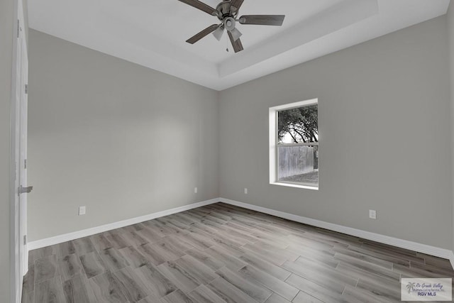 empty room featuring ceiling fan, a raised ceiling, and light wood-type flooring