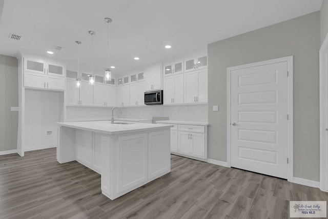 kitchen with pendant lighting, a center island with sink, sink, light hardwood / wood-style flooring, and white cabinetry