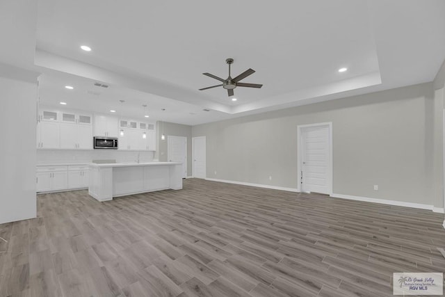 unfurnished living room with ceiling fan, light wood-type flooring, and a tray ceiling